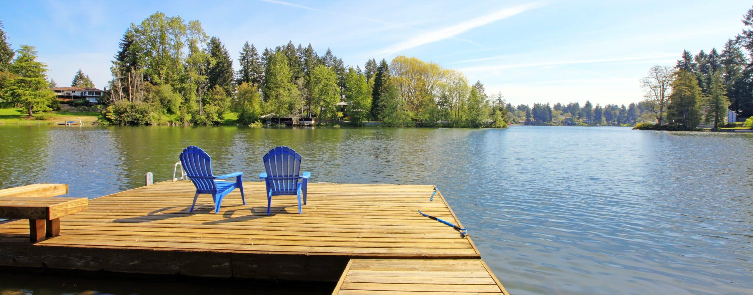 Lake waterfront with pier and two blue chairs.